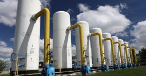 Several gas tanks are arranged in a row on a grassy field outside. Each tank has a gas booster pump attached to it.