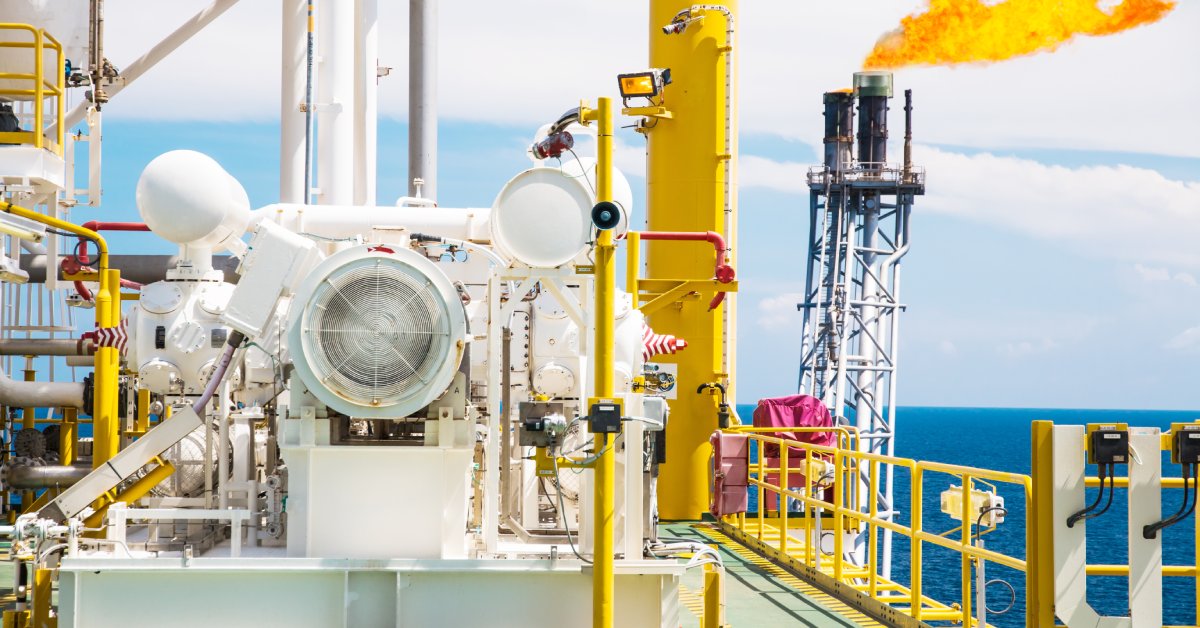 A large gas booster compressor situated on an offshore rig, with flaring in the background producing a large flame.