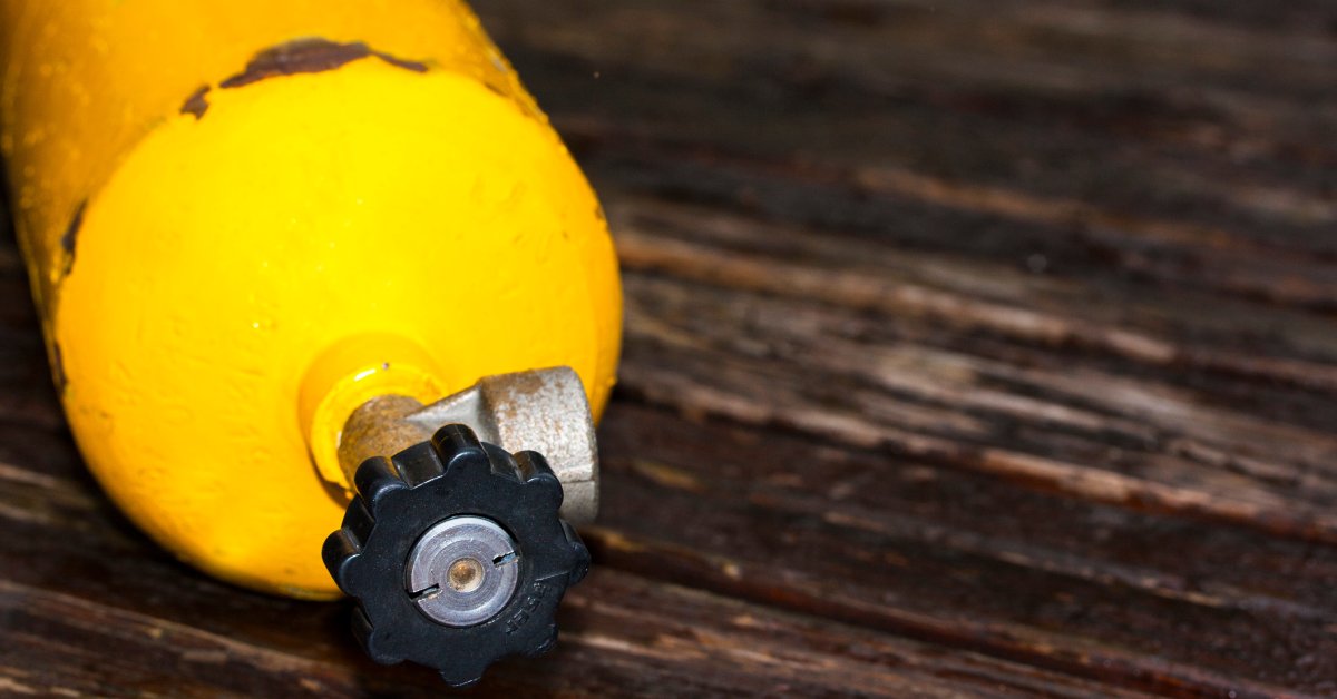 An old, weathered yellow oxygen tank, its paint chipped and faded, resting on a worn wooden surface.